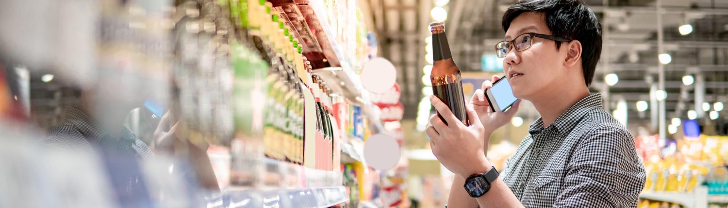 Side view of a man on the phone while looking through the alcohol aisle of a grocery store